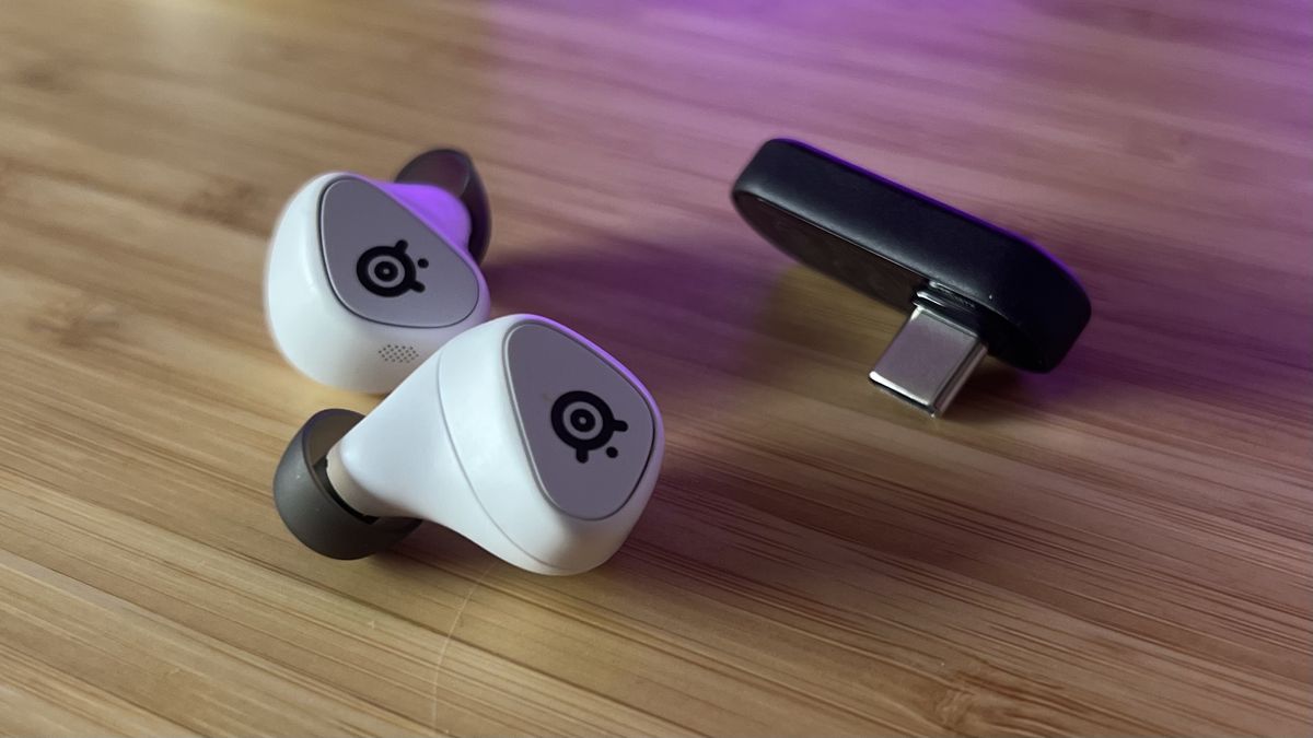 SteelSeries Arctis Game Buds on a wooden desk with USB-C 2.4GHz receiver