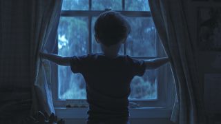 the back of Alex as he opens the curtains at night in Weapons