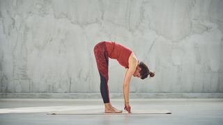 Woman in activewear standing with fingertips touching ground in a fold