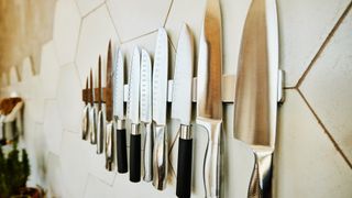 a selection of kitchen knives hanging on a magnetized panel on kitchen wall