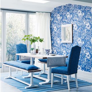 A blue and white dining room with bold floral wallpaper, a blue rug and blue chairs