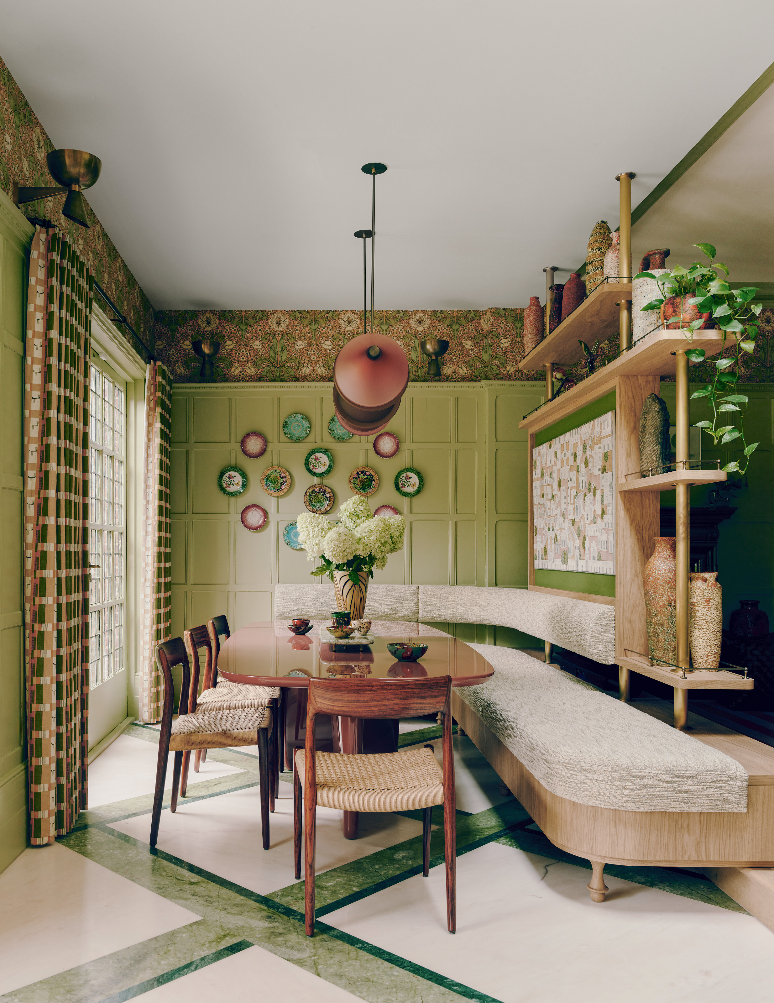 Green paneled dining room with cream and wood banquette seating, wood dining table and chairs, and floral wallpaper