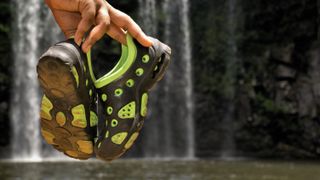 Man holding water shoes by waterfall