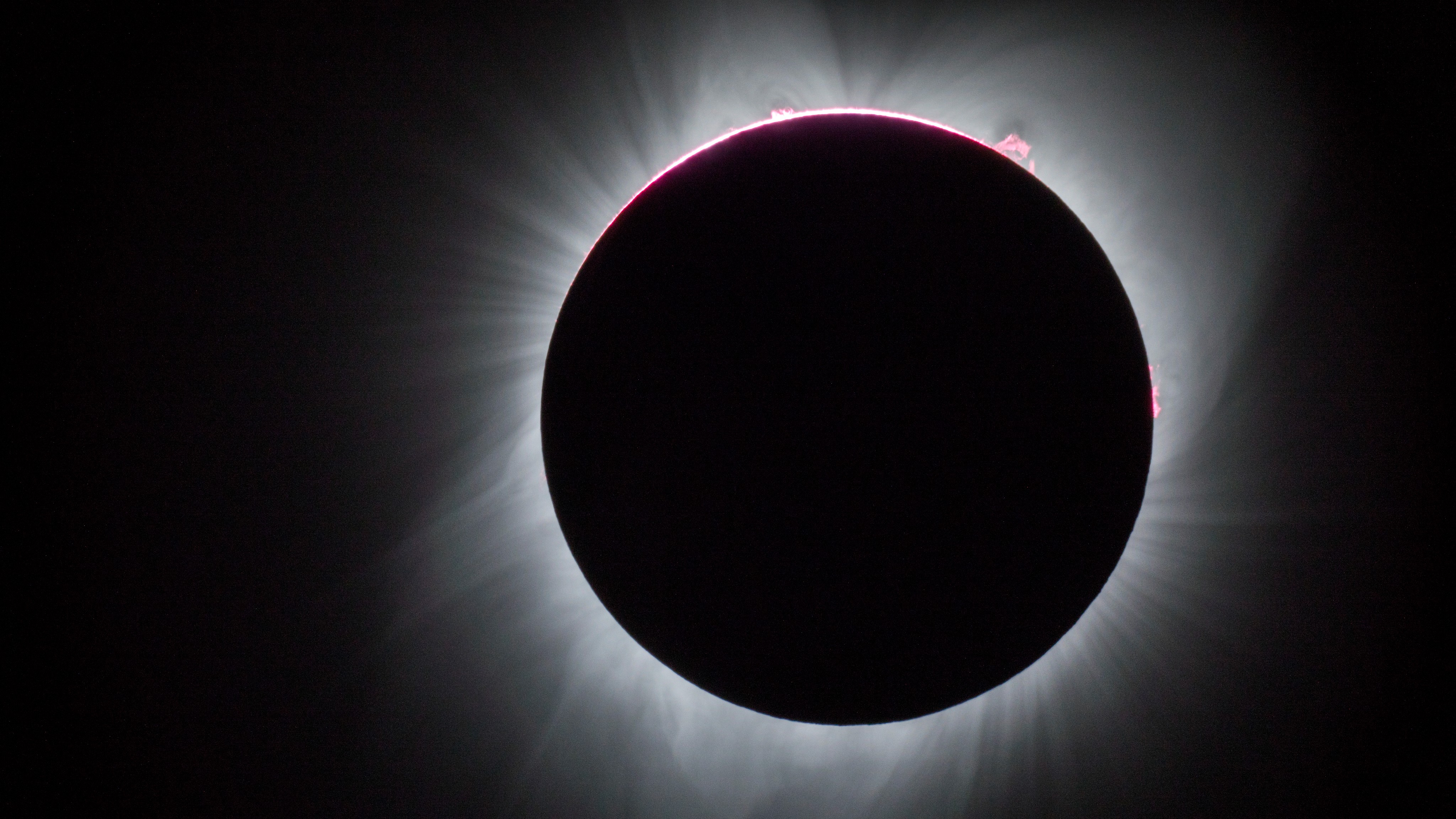 A photograph of a fully eclipsed sun, with white spikes of coronal energy shooting out from behind the moon
