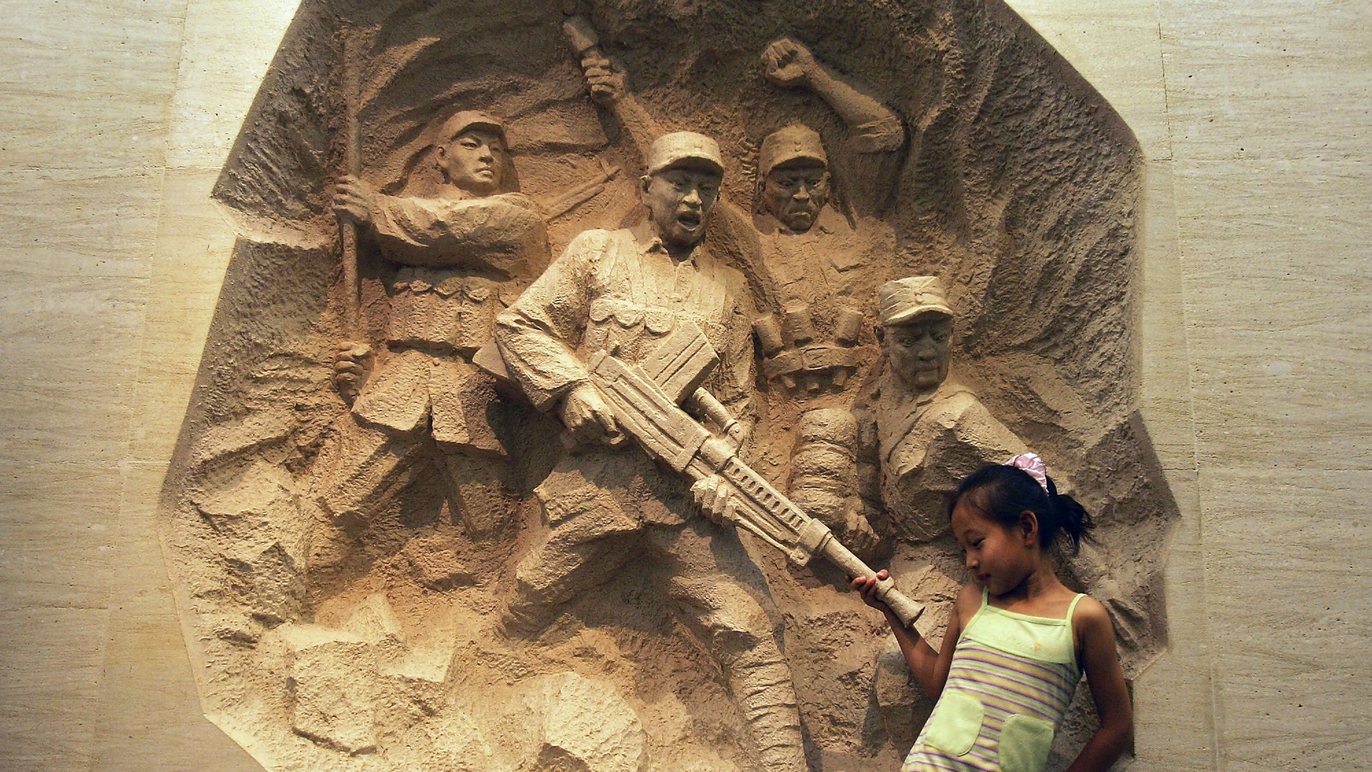 A little girl stands next to a Chinese war memorial
