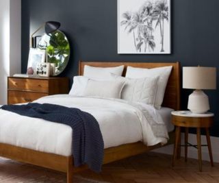 Mid-century modern bed frame against a navy wall.