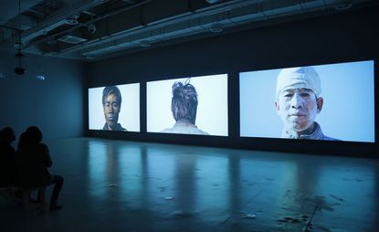 Three large portraits on display in a dark room. 