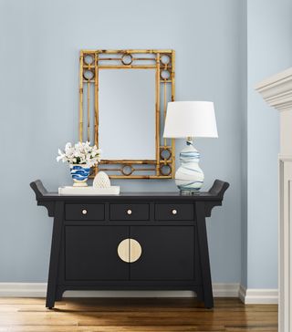 A hallway with walls painting in a light muted blue shade and a navy console table with a mirror above it