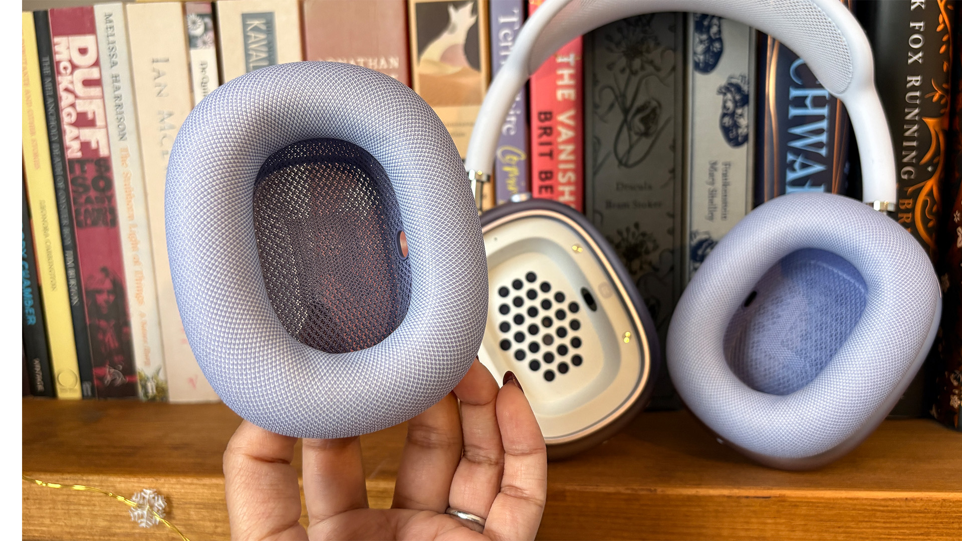 Apple AirPods Max 2 over-ear headphones on bookcase, foam earcup detached and held in hand