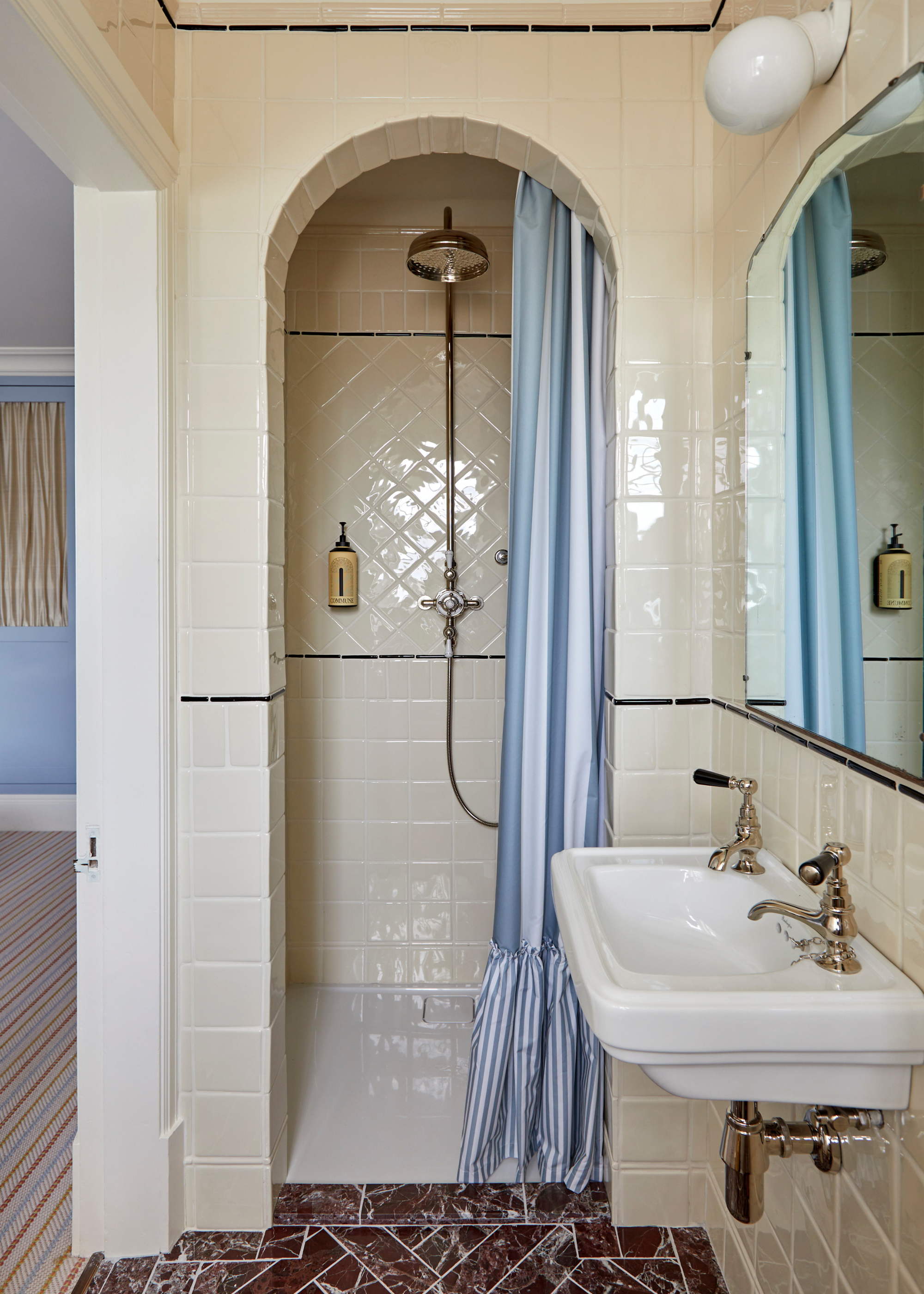 white tiled shower with an arched entrance and a striped blue shower curtain