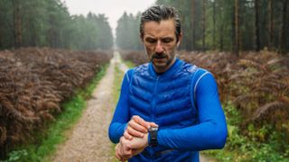 Man checking sports watch while running in forest