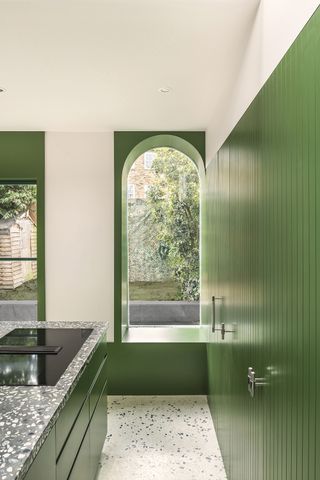 A contemporary colour blocked green kitchen with arched doors