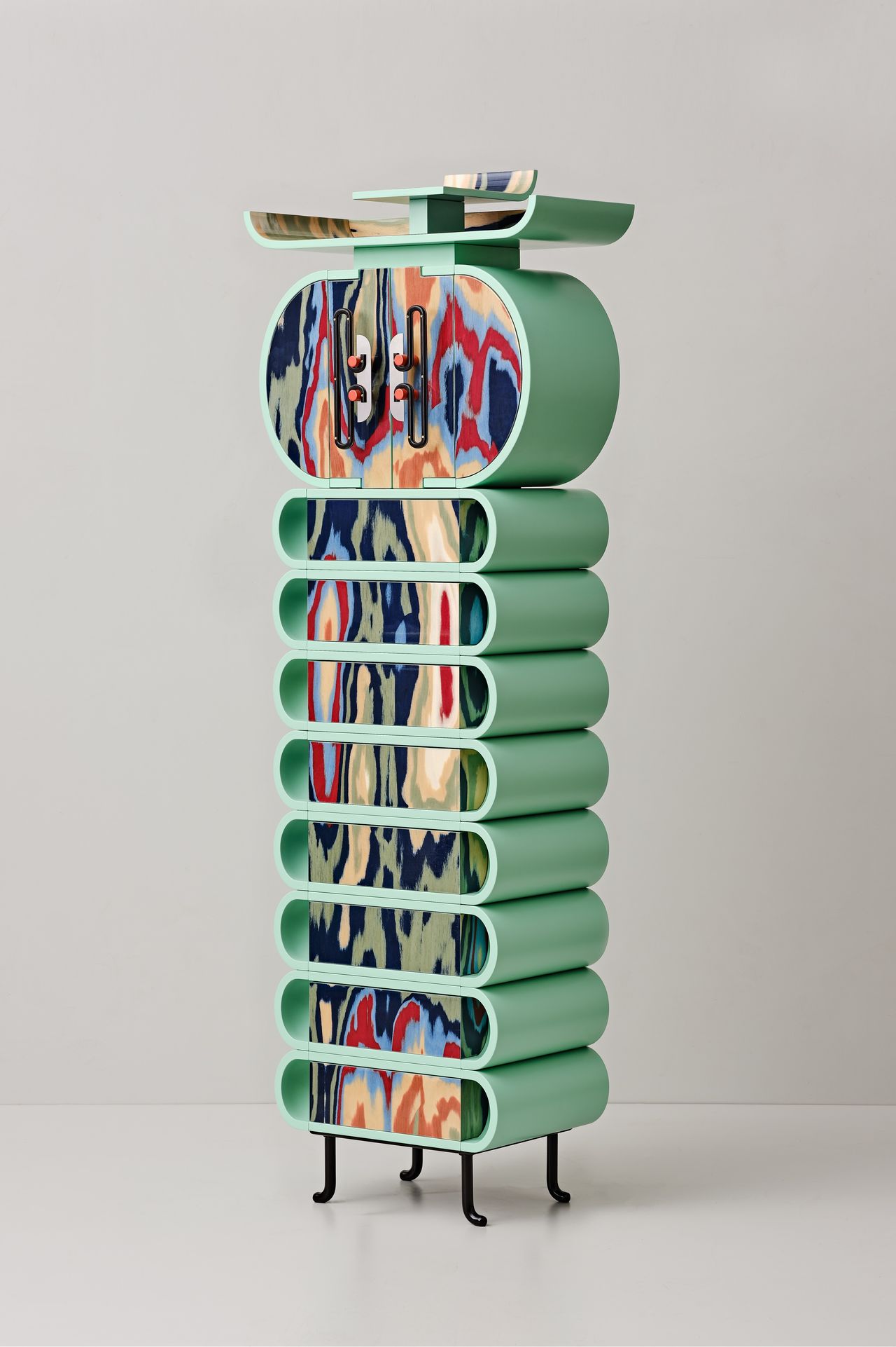 A caterpillar-shaped cabinet in eccentric colors and whimsical shapes stands in an empty grey room.