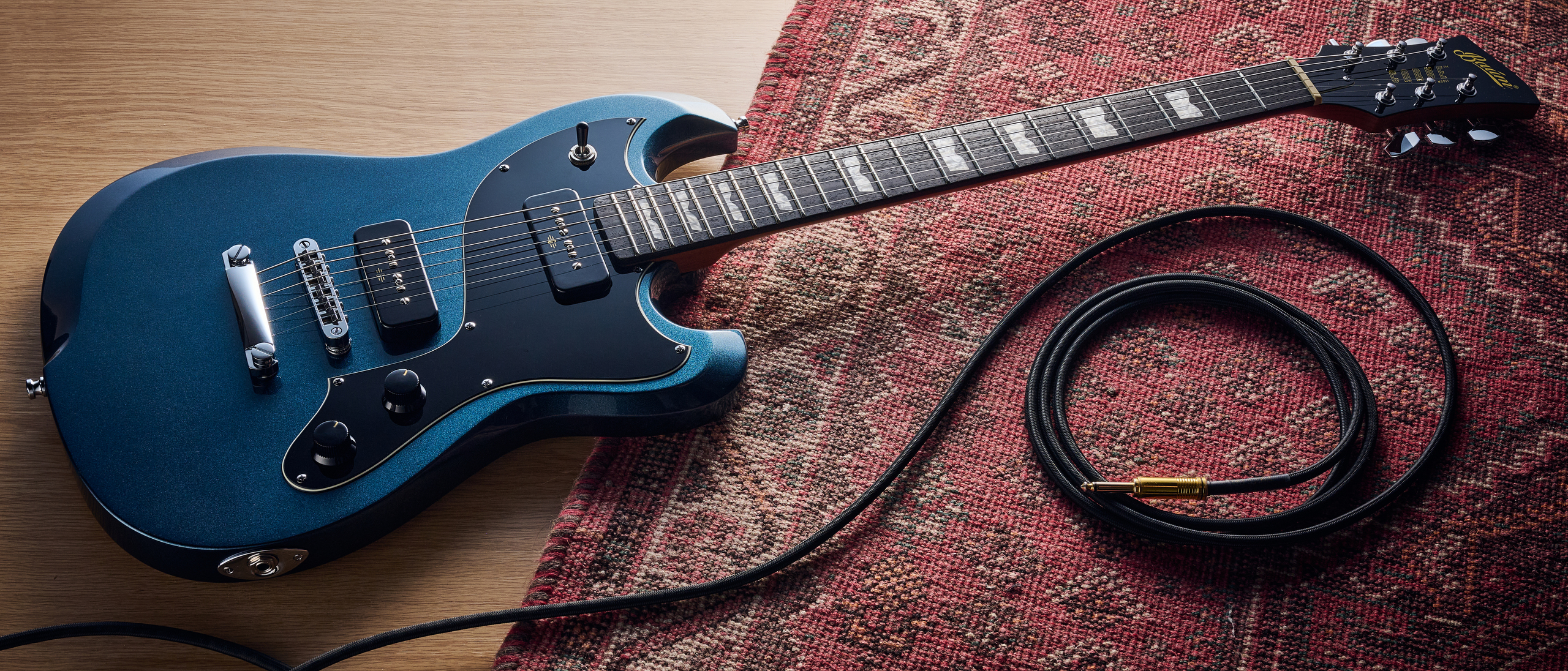 A Baum Carve electric guitar on a rug with a guitar cable coiled nearby