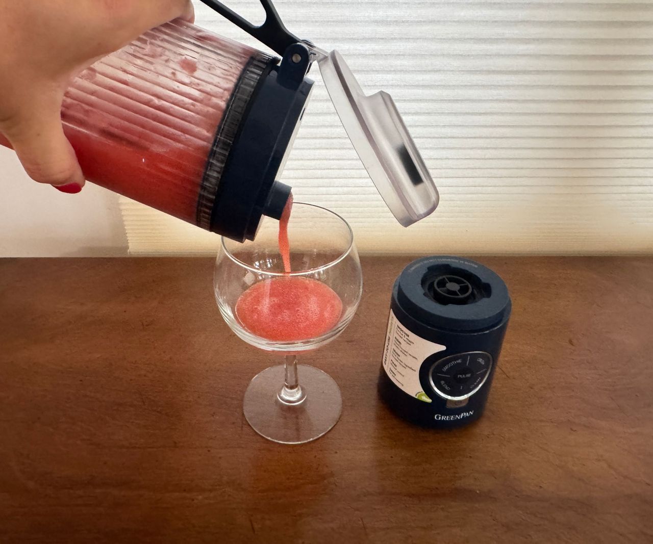 Pouring a pink liquid from a black portable blender into a drinking glass.