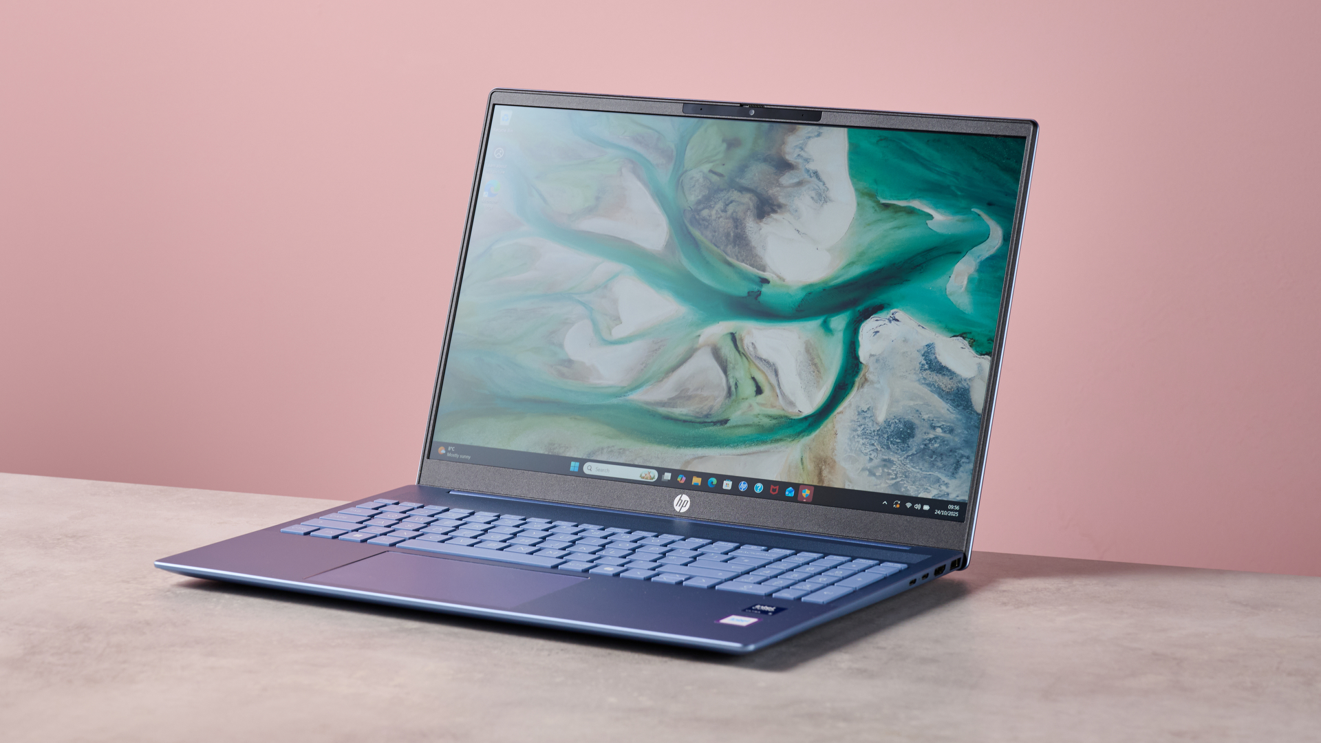 Three-quarter view of HP Pavilion 16 open on desk with pink wall in background