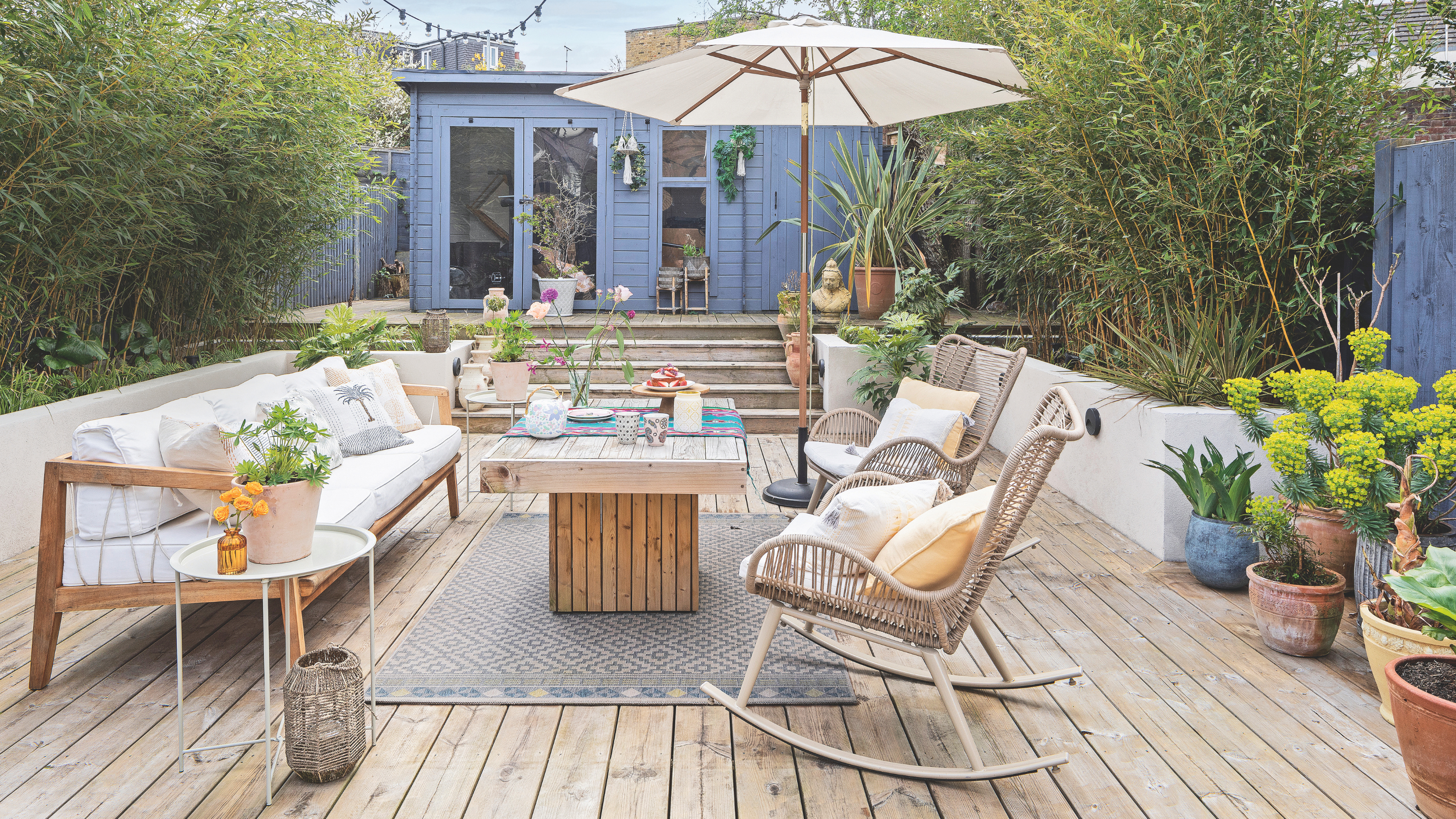 Patio with rattan chairs and wooden table. Potted plants in terracotta pots and a parasol.