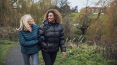Two women walking arm in arm in a park wearing warm jackets