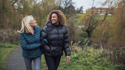 Two women walking arm in arm in a park wearing warm jackets