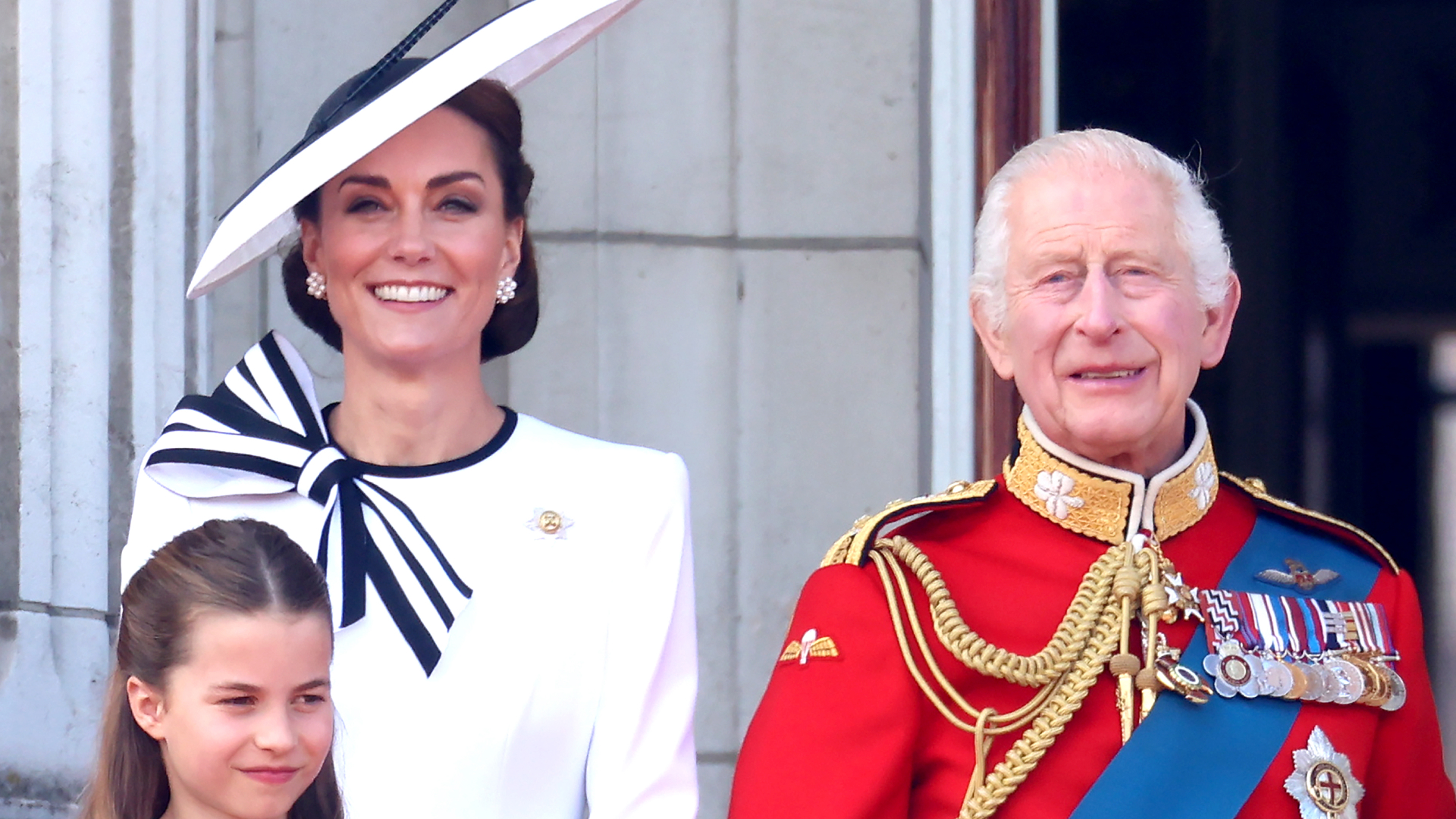 Kate Middleton wears a white dress with navy accents and a matching hat while King Charles wears red military uniform
