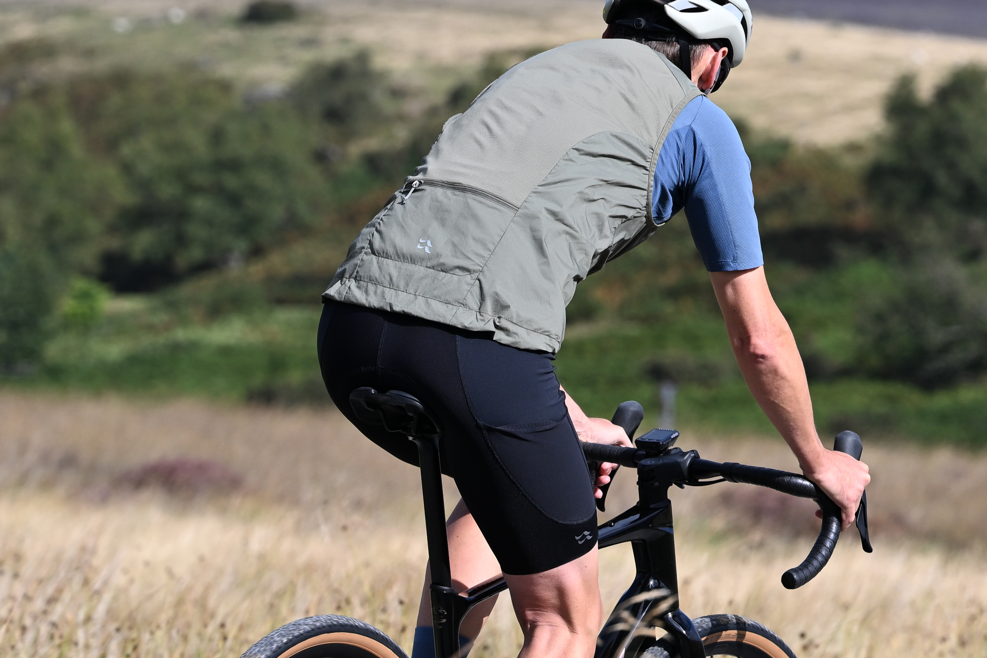 rear view of a man riding a black gravel bike wearing black shorts, blue jersey and green gilet