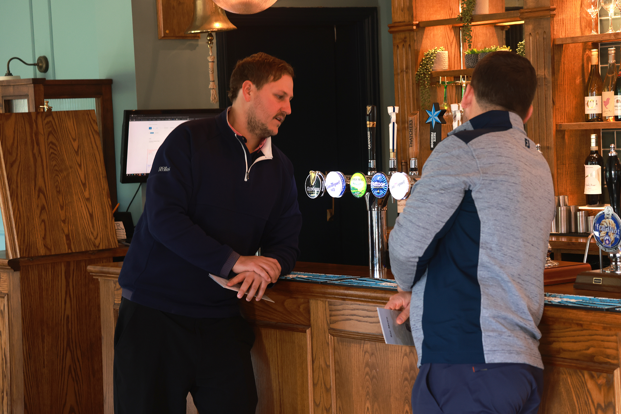 Nick Bonfield and Sam De&#039;Ath talking at the bar in the golf clubhouse, holding their scorecards from their round of golf