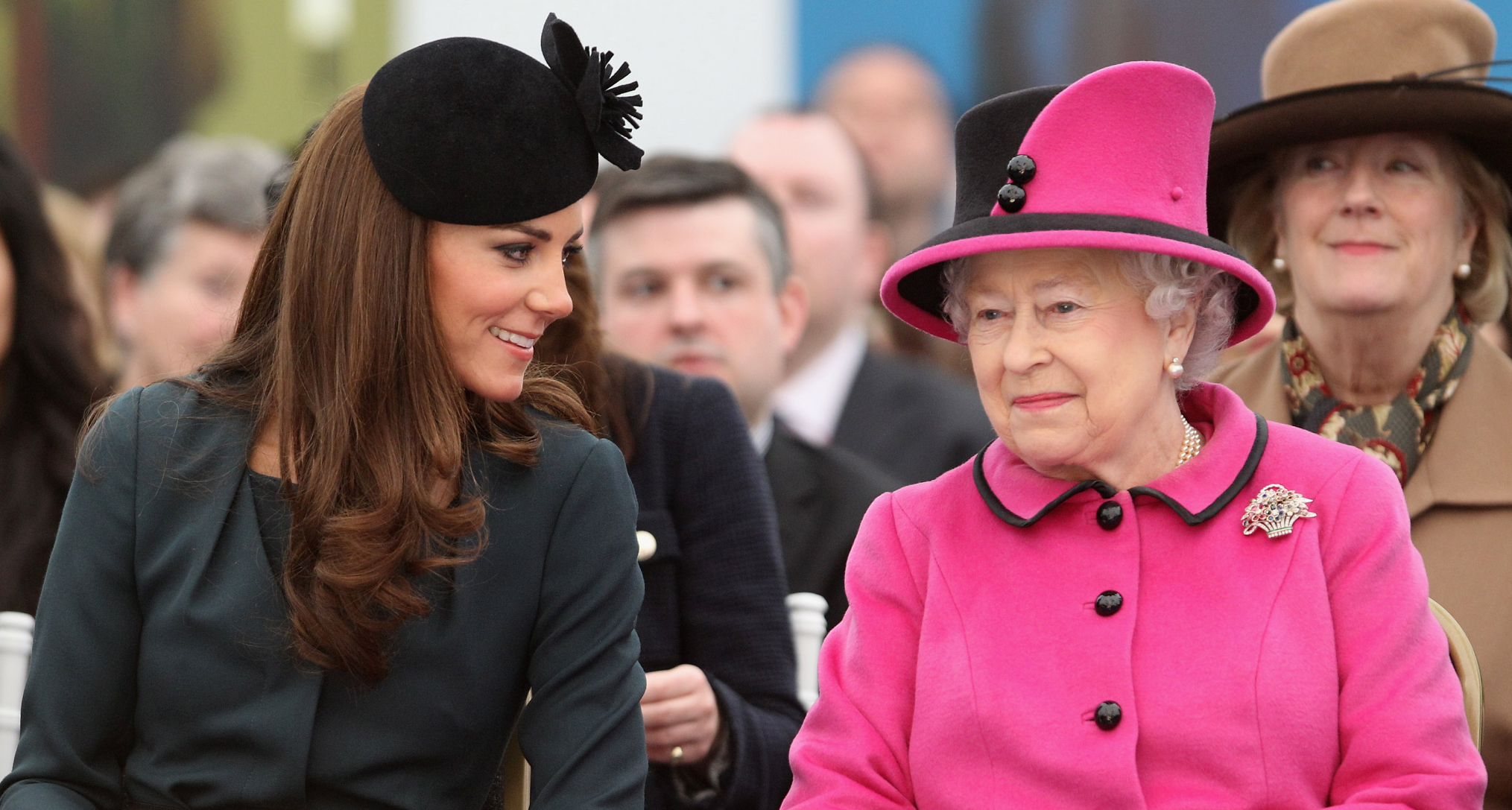 Princess Kate sitting next to Queen Elizabeth wearing a pink suit and smiling