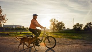 Woman bicycling with dog next to her