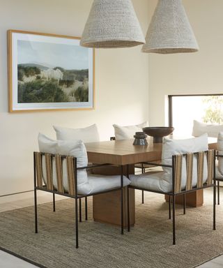 Relaxed dining room with cream painted walls, wooden dining table, chairs, beige rug, two cream textured pendants, artwork on wall