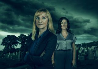 A blue-tinted image of Hannah (Lesley Sharp) and Dubravka (Kazia Pelka) standing in front of a graveyard