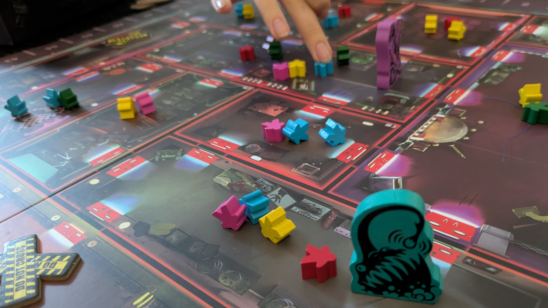 A hand reaches out to grab colorful meeple tokens on the Spooktacular board