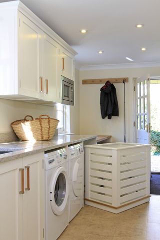 cream and white utility room idea with a moveable laundry basket, washing machine and tumble dryer, and a basket on the worktops