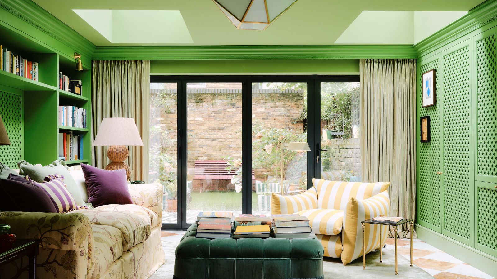 A media room with bright green walls, a light green ceiling with skylights, a wall of doors leading to a garden, and colorful decor. 