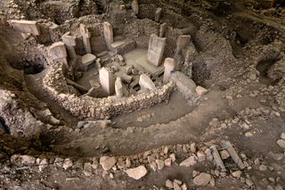 large stone structures rise up out of dusty soil at a dig site