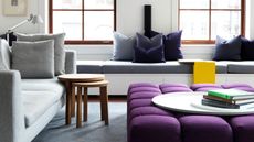gray living with purple upholstered coffee table with large tray and books, a long banquette seat under the window with purple cushions, and a nesting coffee table next to a gray sofa