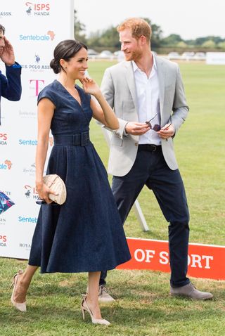 Meghan Markle attends the Sentebale Charity Polo match wearing a low cut dress and tall heels while walking next to Prince Harry