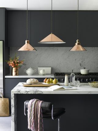 Black matte kitchen with white marble surfaces and low hanging brass lights