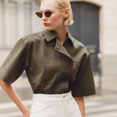 A female model wearing a khaki shirt and white jeans from NET-A-PORTER. 