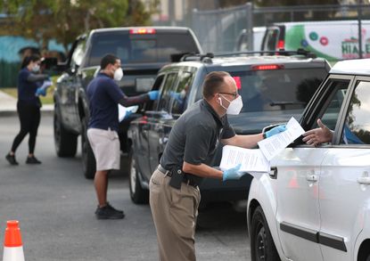 Masked volunteers hand unemployment paperwork to people in a row of cars.