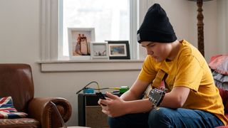 A teen guitarist playing guitar and jamming online using a laptop