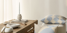 minimalist white candlestick with a slim blue candle on a wooden table with striped blue pillows