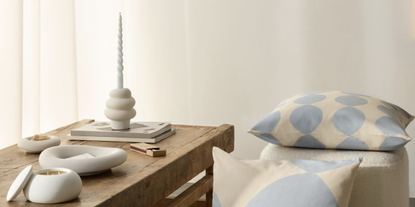 minimalist white candlestick with a slim blue candle on a wooden table with striped blue pillows