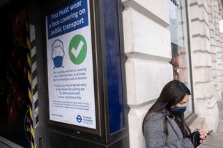 Woman stands outside train station in London with face mask on