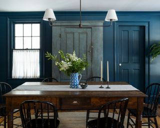 blue dining room with dark blue walls, pale blue distressed cupboard, wooden table with spindle wooden chairs