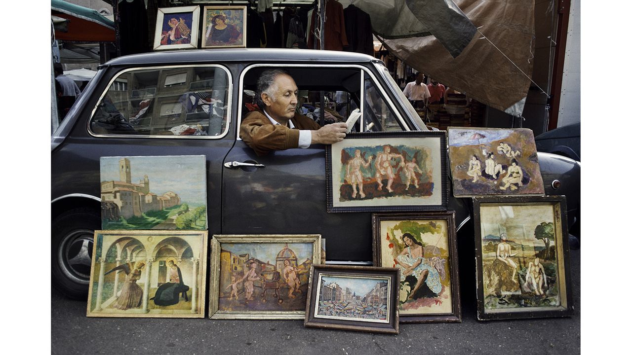 00472_20, Rome, Italy, 1984,ITALY-10041NF. A man displays paintings while he reads in his car.