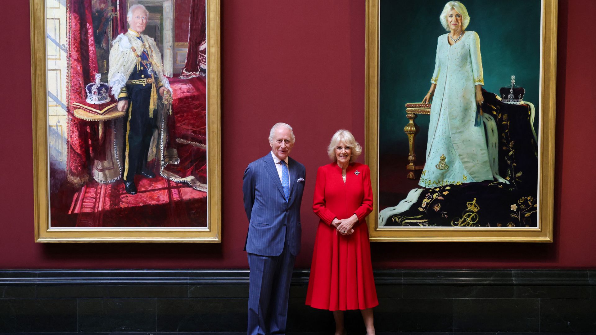 King Charles and Queen Camilla pose in front of their official portraits
