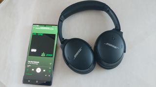 The Bose QuietComfort 45 headphones next to a smartphone showing Spotify
