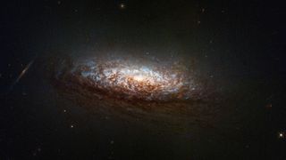 a stunning spiral galaxy hangs dimly in the dark of space; a bright light at its center illuminates nearby gasses, swirling around in shades of pale blues, whites and crisp browns.