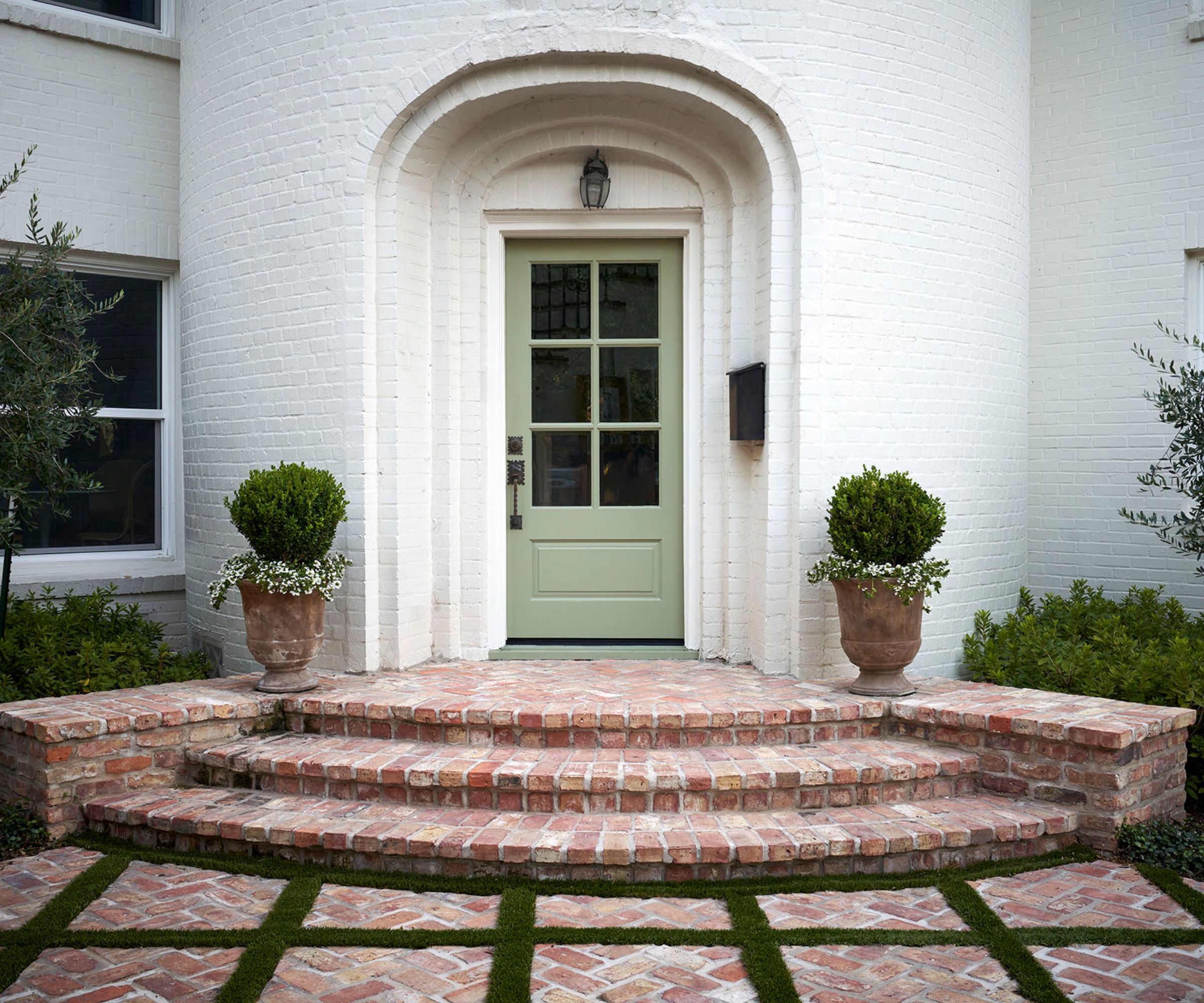 A warm white home exterior with a soft green front door in an arched doorway.