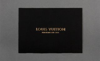 Front view of ﻿Louis Vuitton's black and gold invitation pictured against a grey background